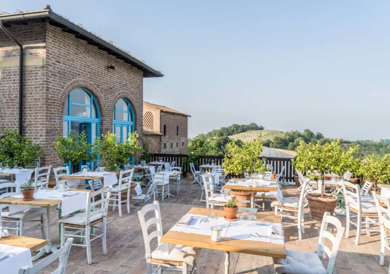 Rooftop dining area with white, wooden tables and chairs, with a brick building to the left