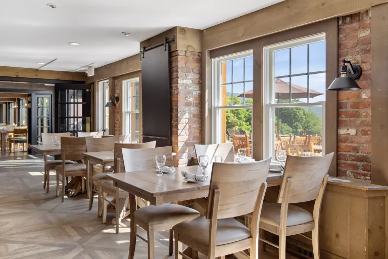 Restaurant dining area with cushioned, beige chairs and exposed brick walls