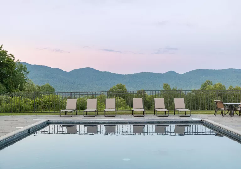 Outdoor pool surrounded by chairs and the sunset in the background