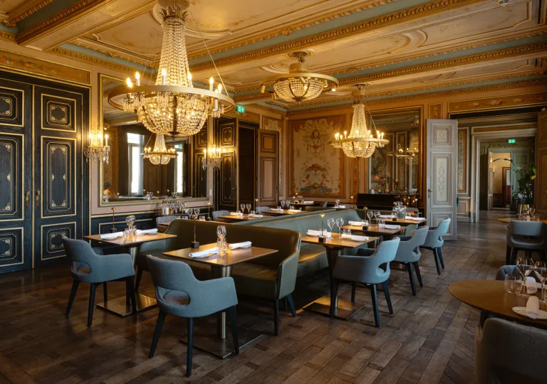 Dimly lit restaurant with wooden tables and gray, cushioned chairs