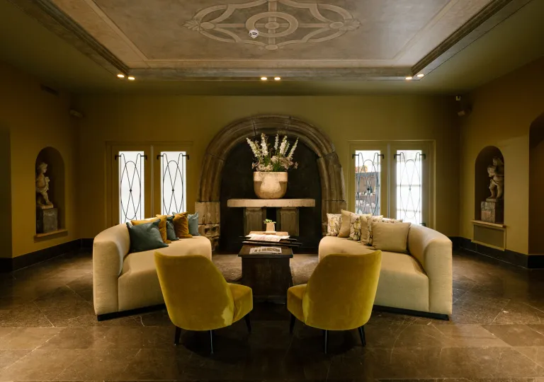 Dimly lit lounge area with beige, cushioned sofas and sculptures along the walls