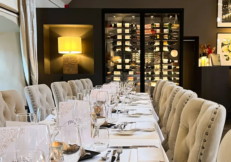 Restaurant dining room with a long dining table and cushioned, beige chairs