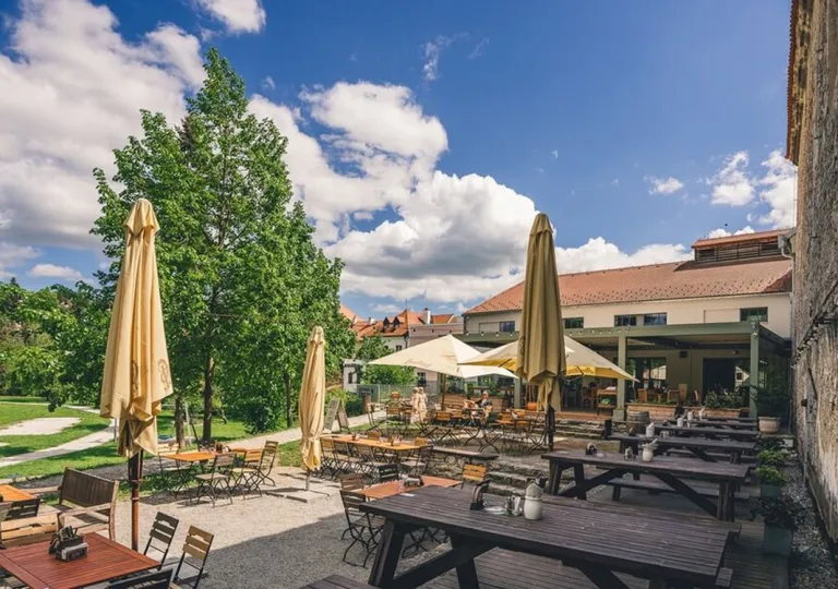The outdoor terrace restaurant, featuring large beige umbrellas and wooden picnic tables at Boutique Hotel Latrán in Český Krumlov, Czech Republic.