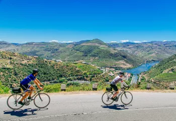 Two bikers riding on a road along the Douro River.
