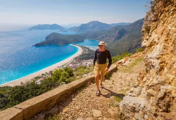 Guest walking along rocky mountainside, ocean, beach, town below.