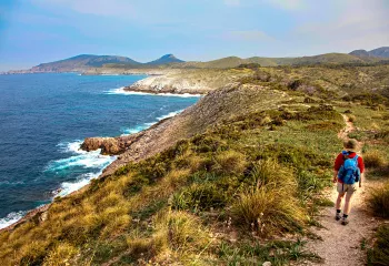 Guest walking beside ocean, towards golden hilly vista.