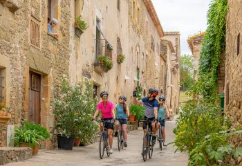 Group of 4 people riding their bikes in an alleyway of a rustic town, surrounded by stone buildings