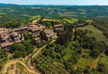 Sky view of brown brick buildings surrounded by a valley of trees and crops