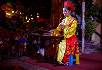 Woman playing a traditional instrument while wearing a traditional outfit