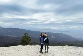 Two women standing on top of a cliff, smiling while holding walking poles