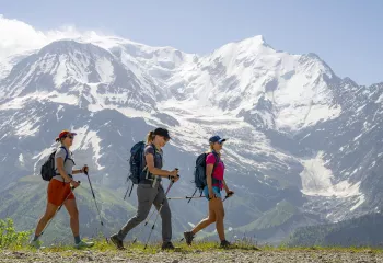 Three women walking on a dirt trail with snow-capped mountains in the background