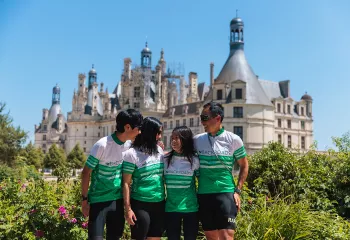 Family in white and green biking jerseys standing in front of a rustic, church-like building