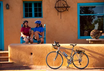 Two women sitting in front of an orange house, with a bike parked out front