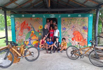 Group of people smiling in front of an art mural with two bikes on either side