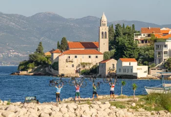Group of people holding bikes over their heads, with a town and ocean in the background