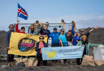 Group of people standing by the ocean, holding up large banners and a flag of Iceland