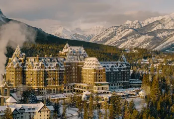 Large, brown hotel building in the middle of a snow and tree-covered valley