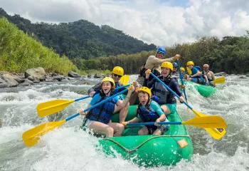 Two groups of families on green rafts, paddling in a river