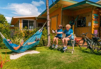 Man laying down on a hammock with two women sitting on wooden stools next to him