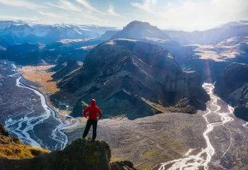 Person standing on a cliff looking out towards tall mountains