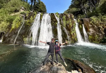 Man and woman with their arms open in front of a waterfall