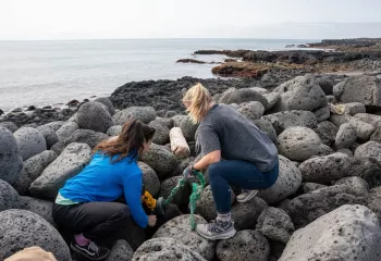 Two women kneeling on large rocks by the ocean