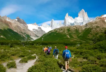 Group of people hiking on a grassy valley with snowy mountains in the distance