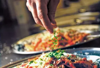 Italian chef sprinkling herbs onto pasta