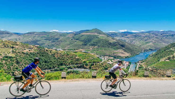Two bikers riding on a road along the Douro River.