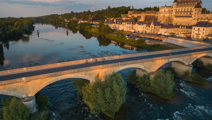 Bird's eye shot of cyclists over Loire River during sunset.  Château Royal d'Amboise behind.