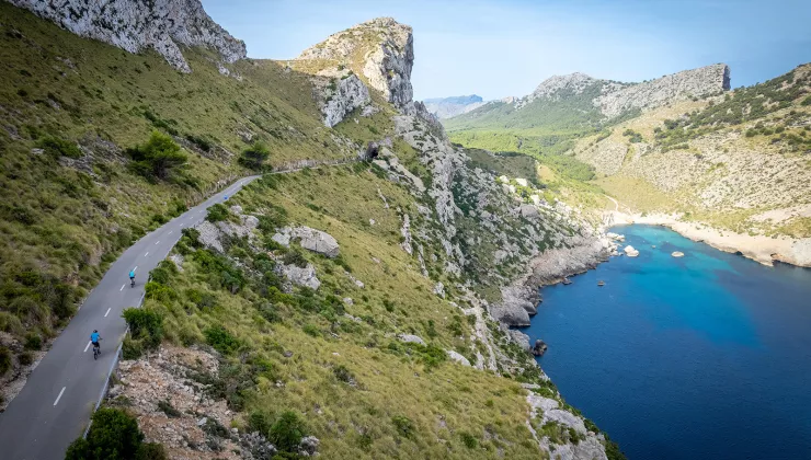 Two bikers riding around a bend on the coast of Mallorca.