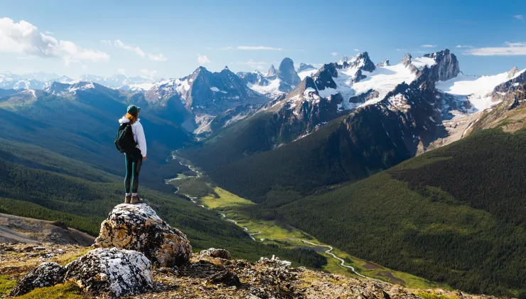 Guest standing on rocky hilltop, looking towards larger mountains.