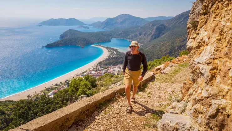 Guest walking along rocky mountainside, ocean, beach, town below.