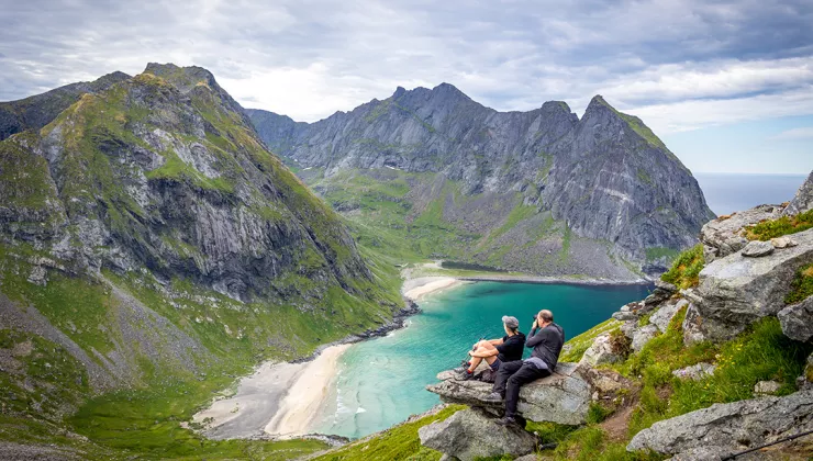 Man and woman on a rocky cliff, looking out to towards larger mountains an a beach