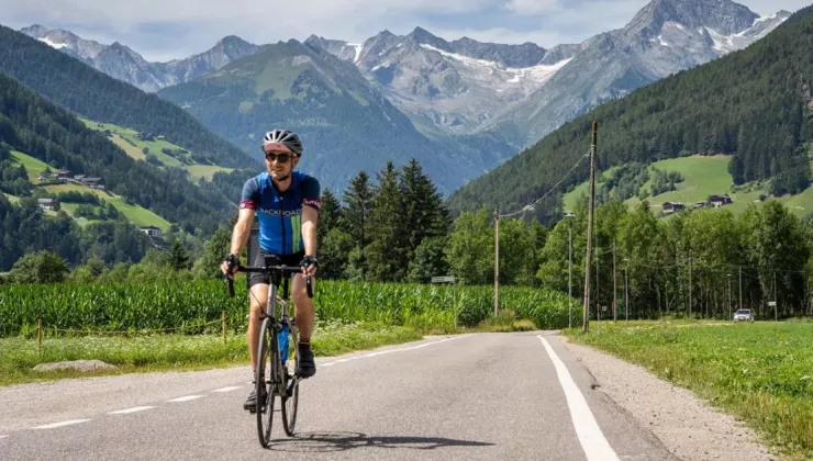 Man biking on an empty road with large grass valleys and mountains in the background