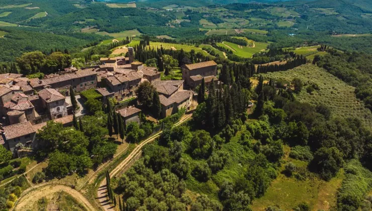 Sky view of brown brick buildings surrounded by a valley of trees and crops