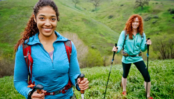 Two women with walking poles on top of a grassy hill