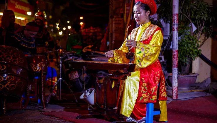 Woman playing a traditional instrument while wearing a traditional outfit