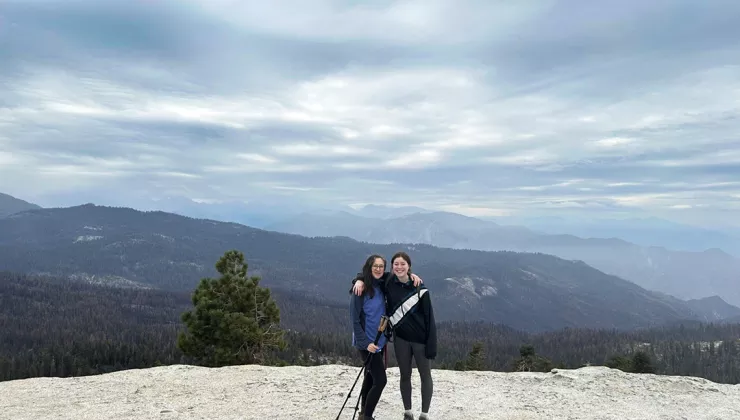 Two women standing on top of a cliff, smiling while holding walking poles