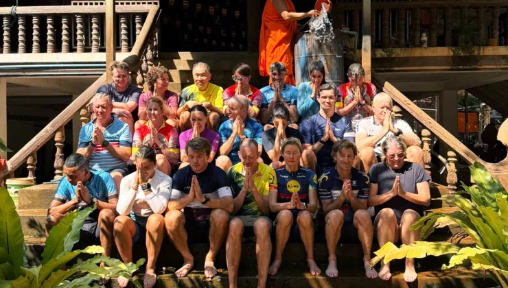 Group of people sitting on a flight of stairs, with a monk on top throwing water on them