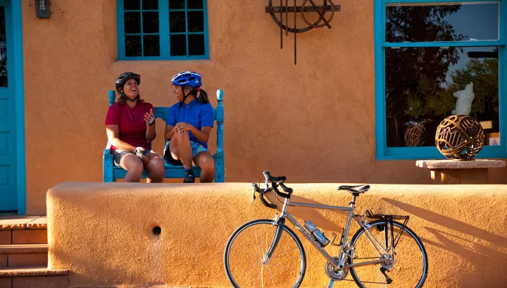 Two women sitting in front of an orange house, with a bike parked out front