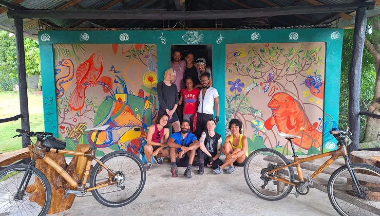 Group of people smiling in front of an art mural with two bikes on either side