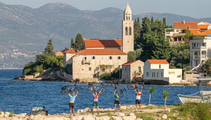 Group of people holding bikes over their heads, with a town and ocean in the background