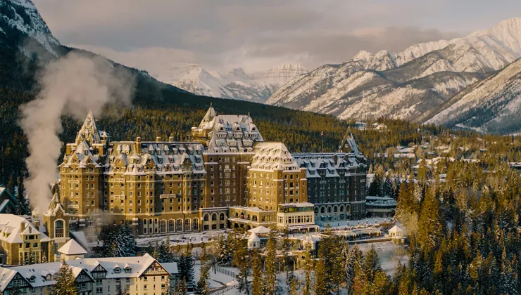 Large, brown hotel building in the middle of a snow and tree-covered valley