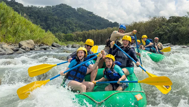 Two groups of families on green rafts, paddling in a river