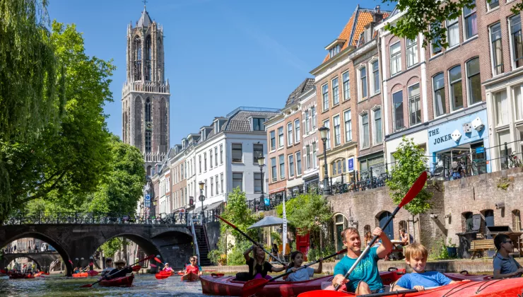 People paddling in red kayaks in a town river