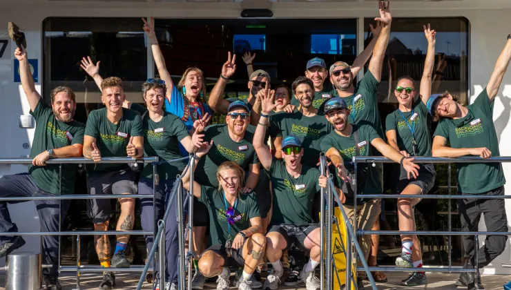 Group of people wearing green t-shirts, smiling with their arms in the air