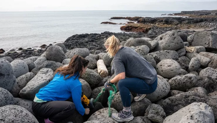 Two women kneeling on large rocks by the ocean