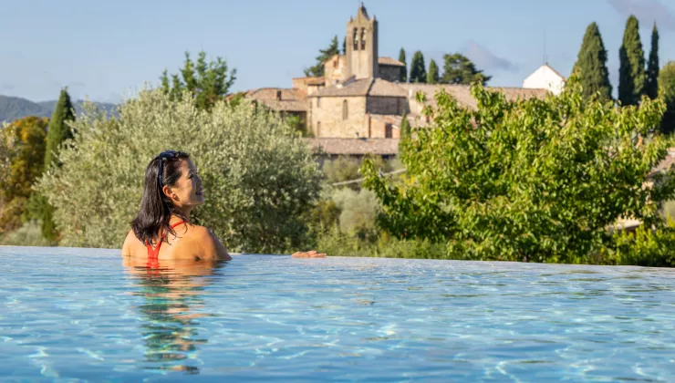 Woman leaning on the edge of an infinity pool, looking out towards a stone castle