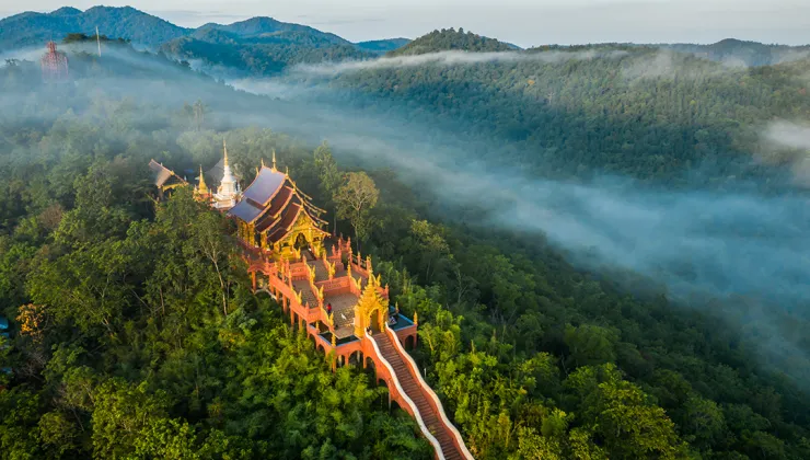 Large Thai temple at the top of a mountain, surrounded by thick forrest